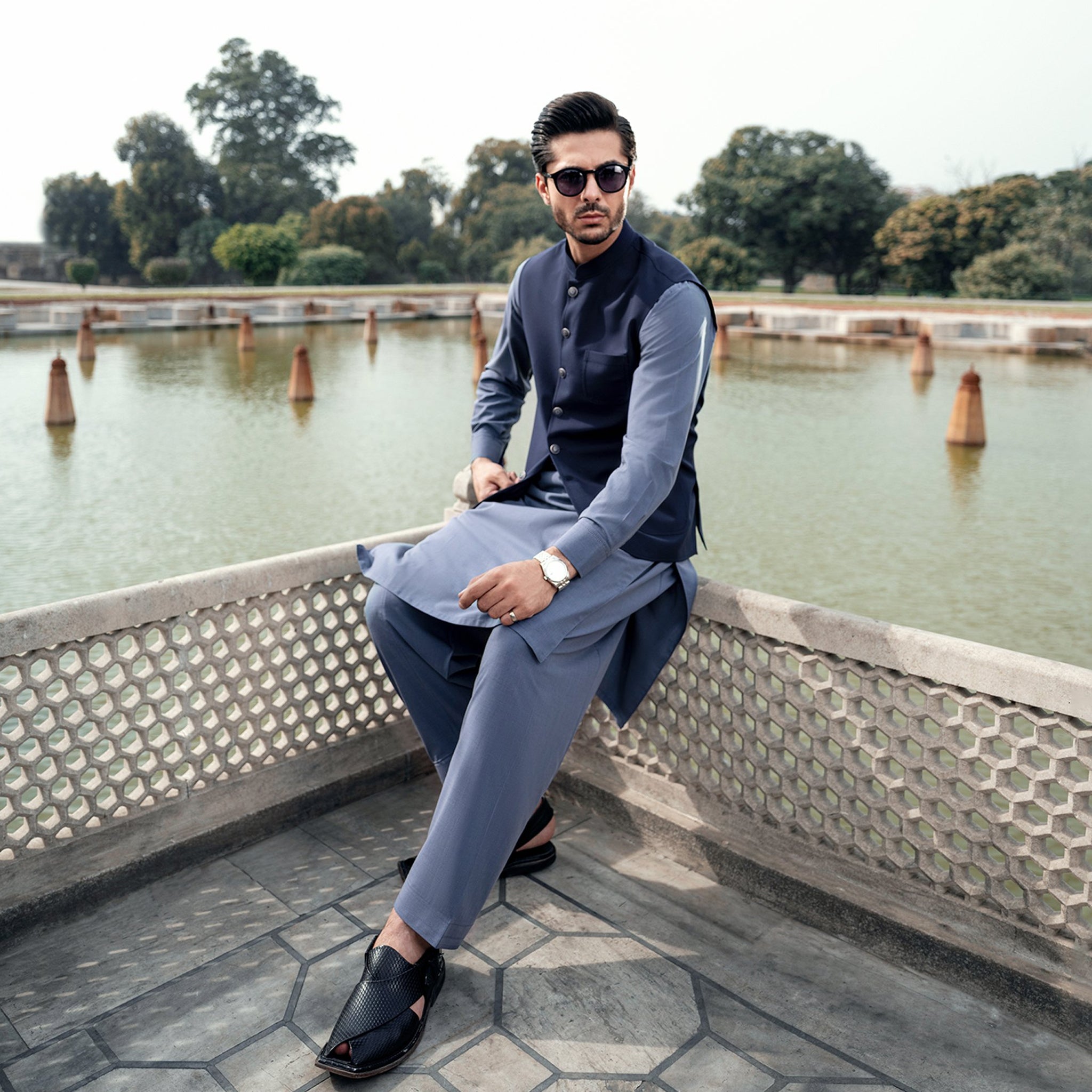 Man wearing a blue shalwar qameez and waistcoat beside a historic pool